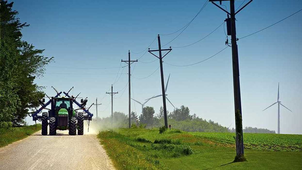A farm tractor driving down a dirt road next to green farm fields