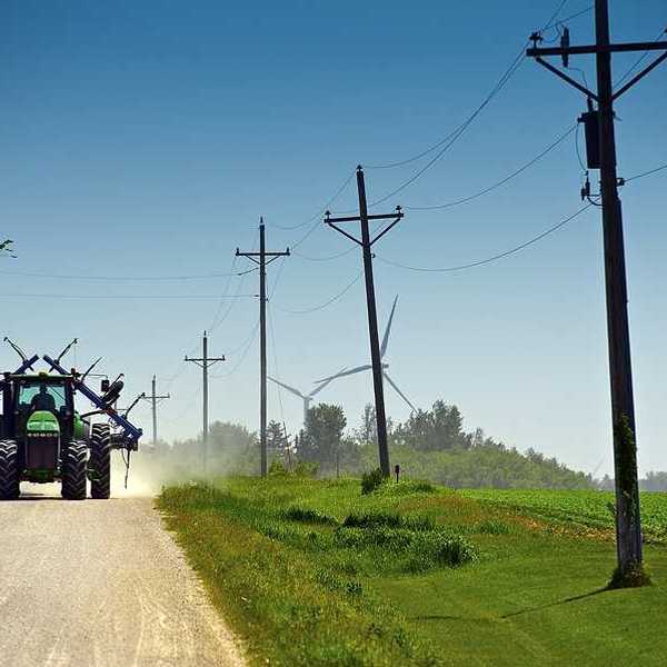 A farm tractor driving down a dirt road next to green farm fields