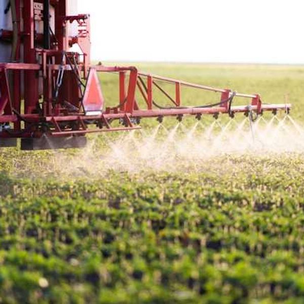 A farm tractor spraying pesticide on a field