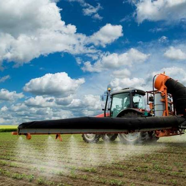 A farm tractor spraying pesticides on a field under a blue sky