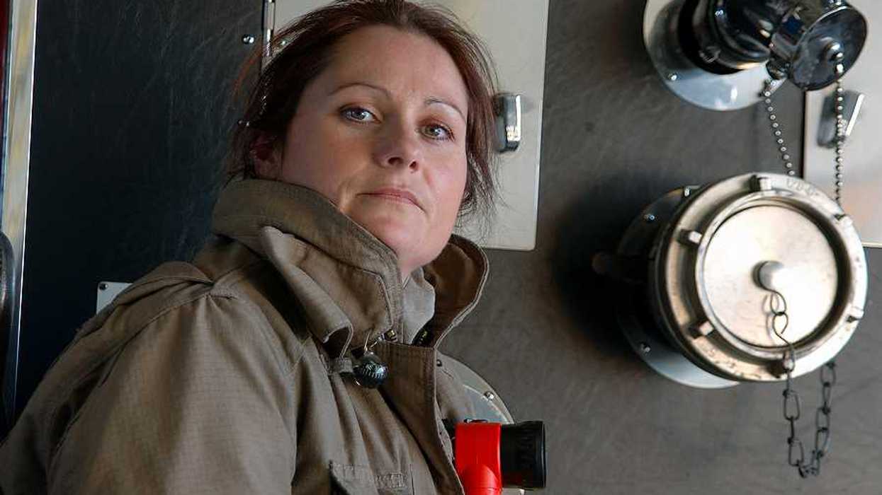 A female firefighter standing next to a fire engine