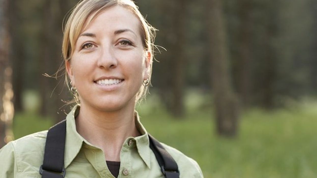 A female hiker in a green shirt with a black backpack looking into the camera.