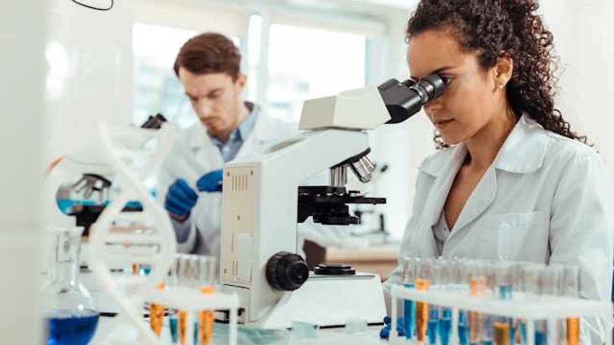 A female scientist standing at a lab table looking into a microscope