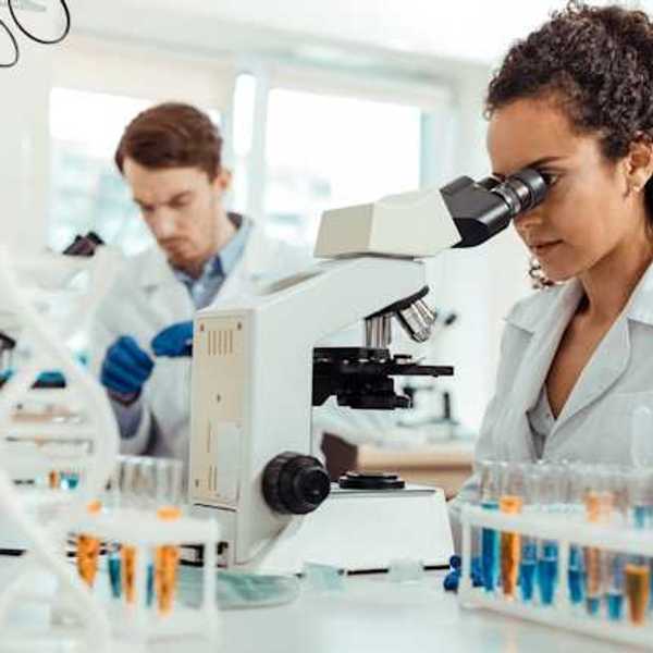 A female scientist standing at a lab table looking into a microscope