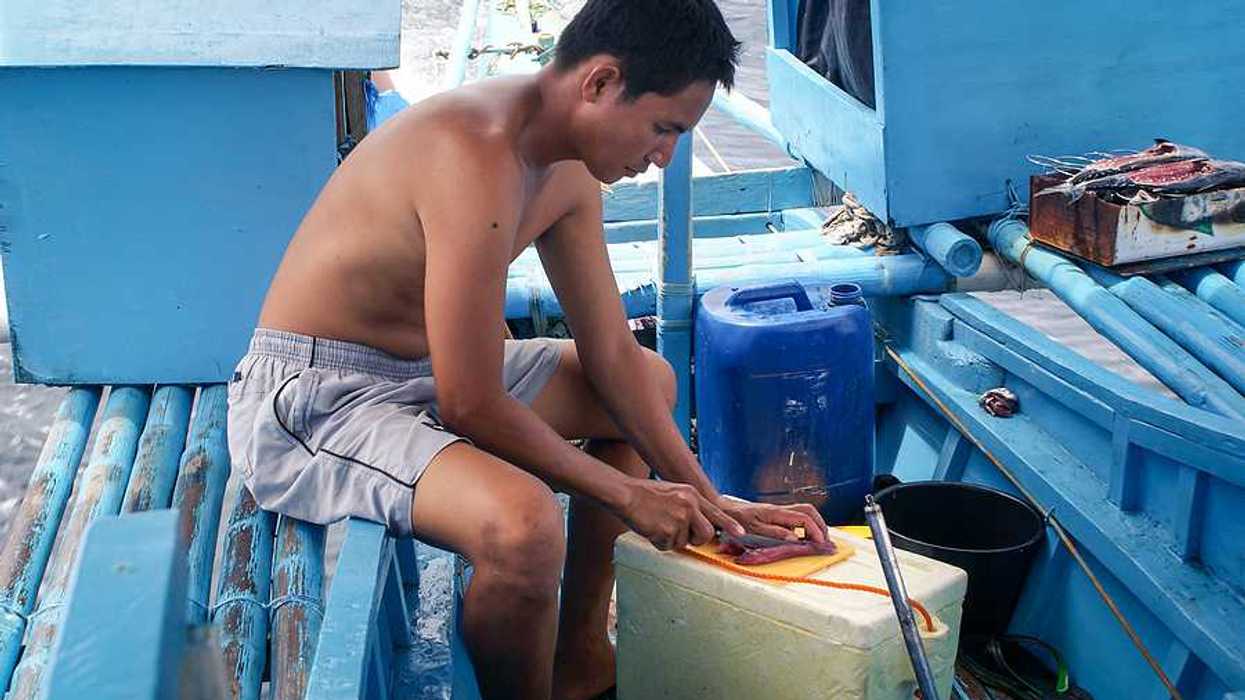 A filipino fisherman filleting a fish on his boat