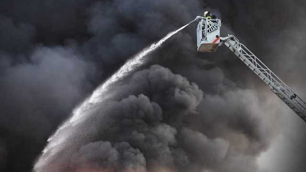 A firefighter directing water on a building fire with black smoke billowing into the air