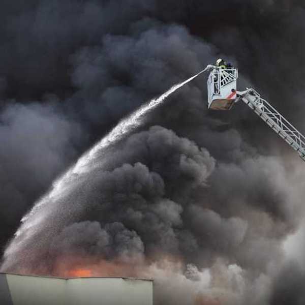 A firefighter directing water on a building fire with black smoke billowing into the air
