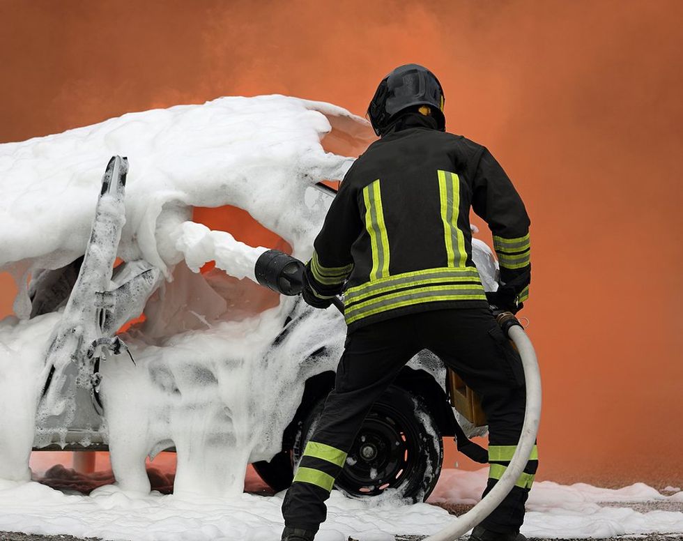 A firefighter spraying toxic foam with PFAS on a car.