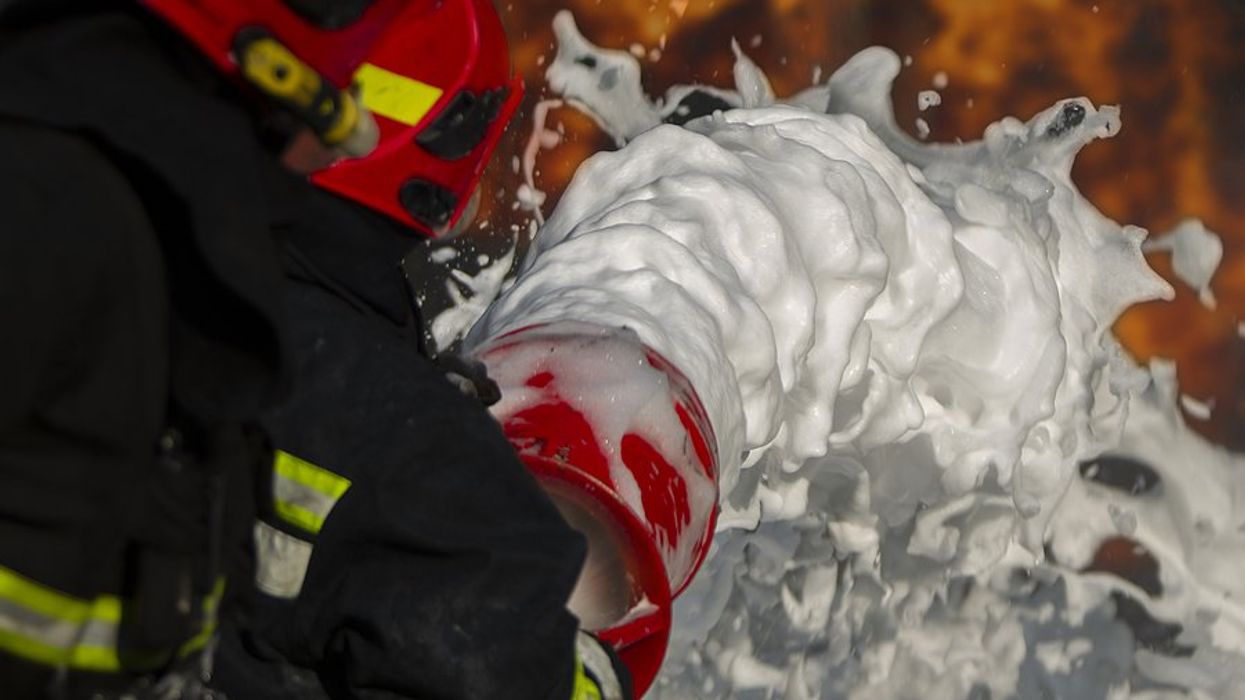 A firefighter spreading firefighting foam on flames