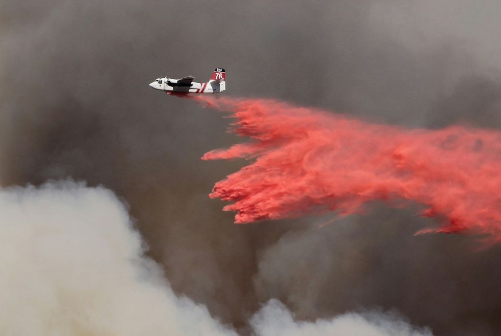 A firefighting plane drops orange retardant above smoky skies.