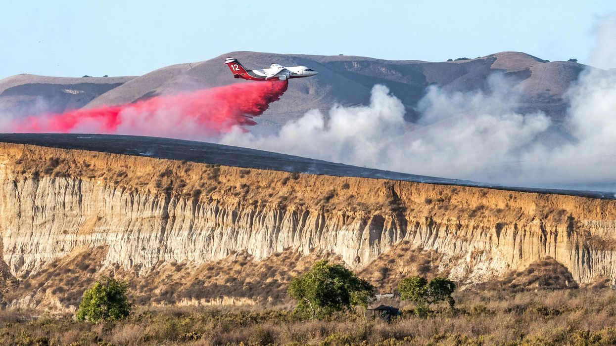 A firefighting plane releasing fire retardant on a hillside next to a riverbed.