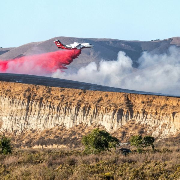 A firefighting plane releasing fire retardant on a hillside next to a riverbed.