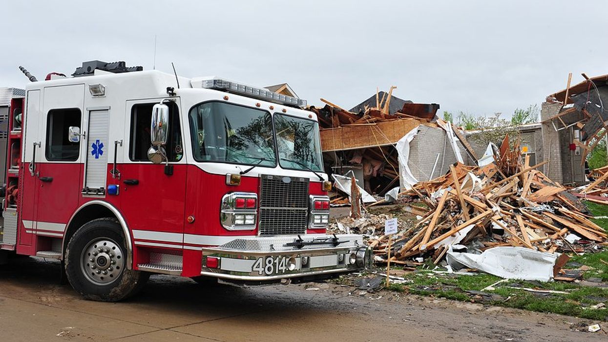 A firetruck parked in front of a home destroyed by a tornado