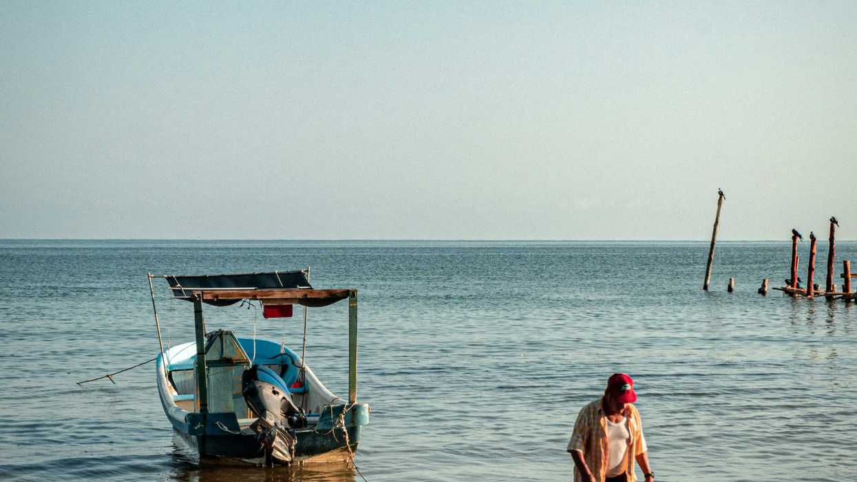 a fisherman sitting on the shore of a beach next to a boat