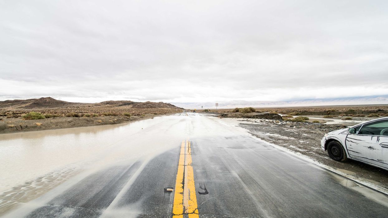 A flooded highway with a white car pulled over in the mud.
