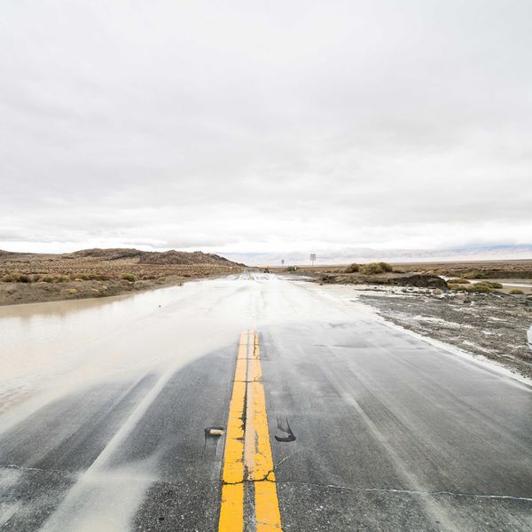 A flooded highway with a white car pulled over in the mud.
