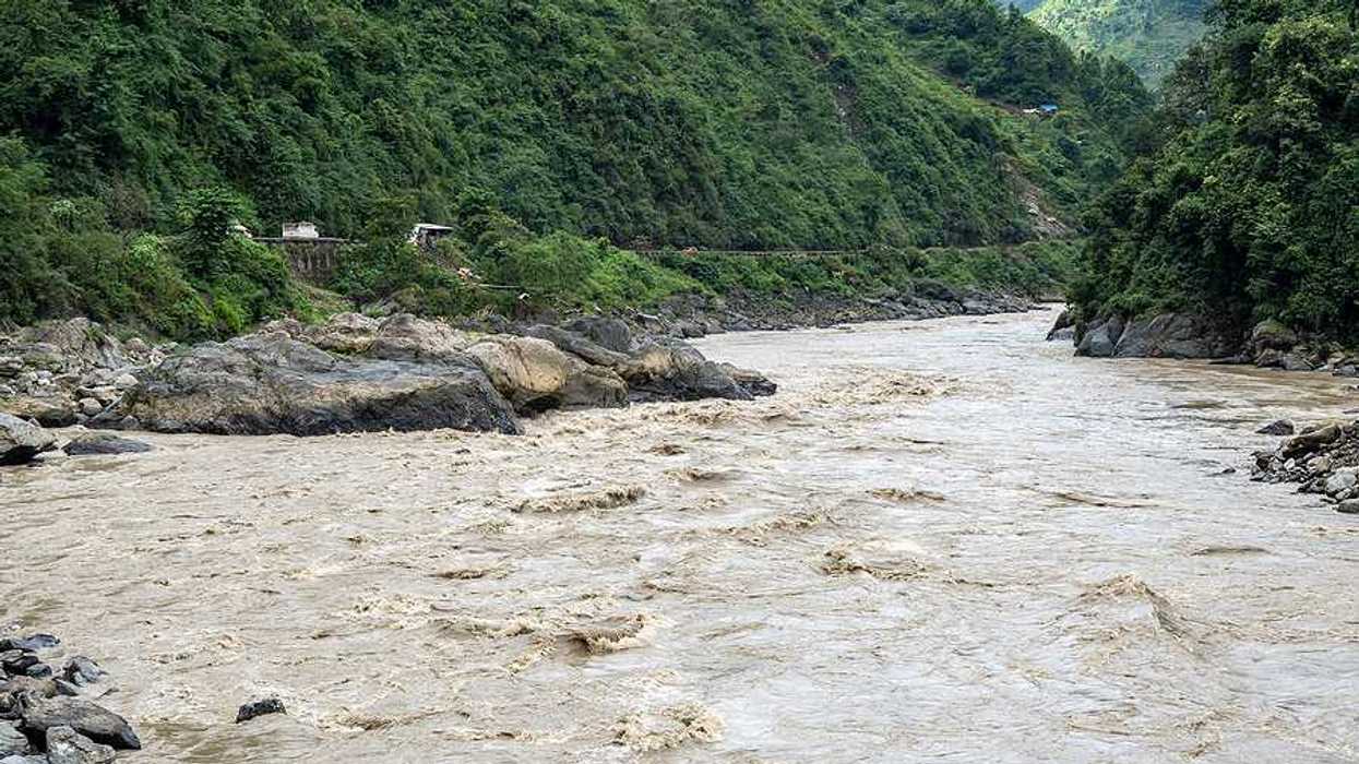 A flooded river lined with rocks in a valley between two green hills