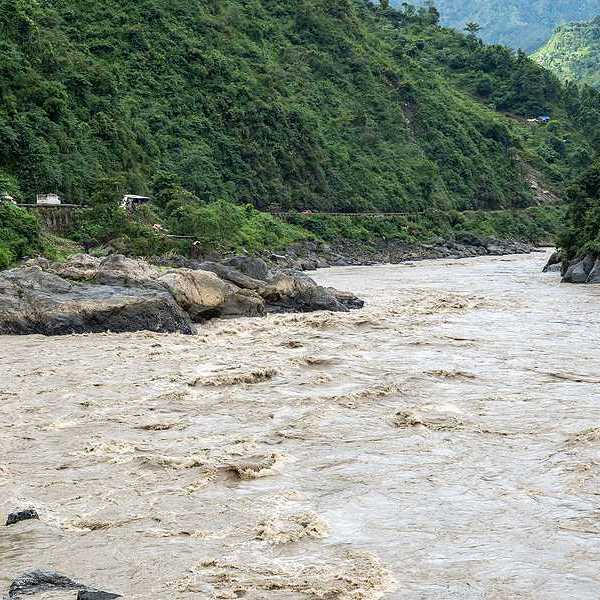 A flooded river lined with rocks in a valley between two green hills