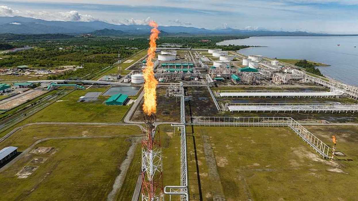 A fracking tower flaring with flames with a refinery in the background