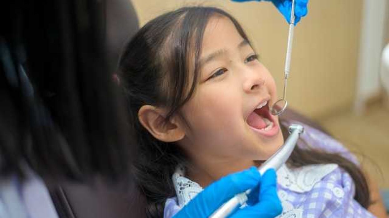 A girl sitting in a dental chair with a dental mirror in her mouth