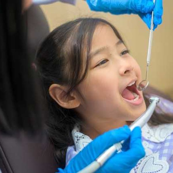 A girl sitting in a dental chair with a dental mirror in her mouth