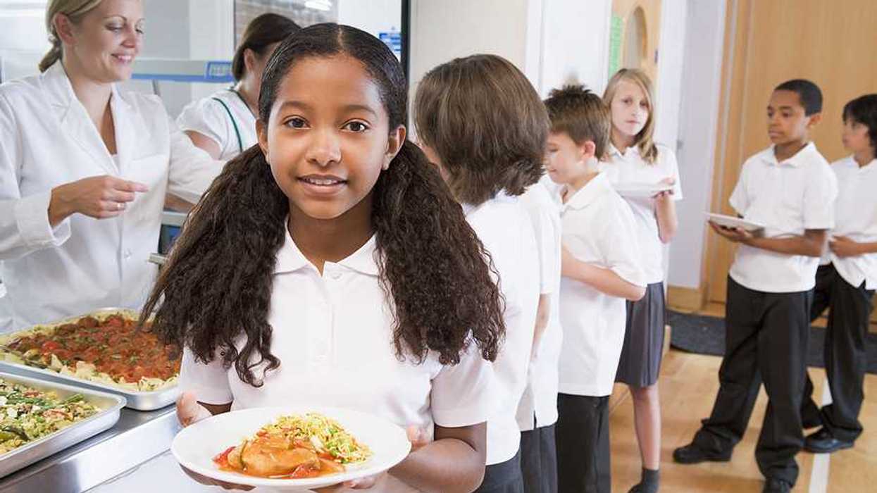 A girl walks away from a cafeteria school line with a plate of food