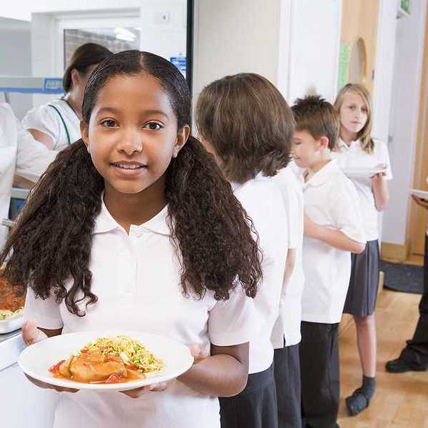 A girl walks away from a cafeteria school line with a plate of food
