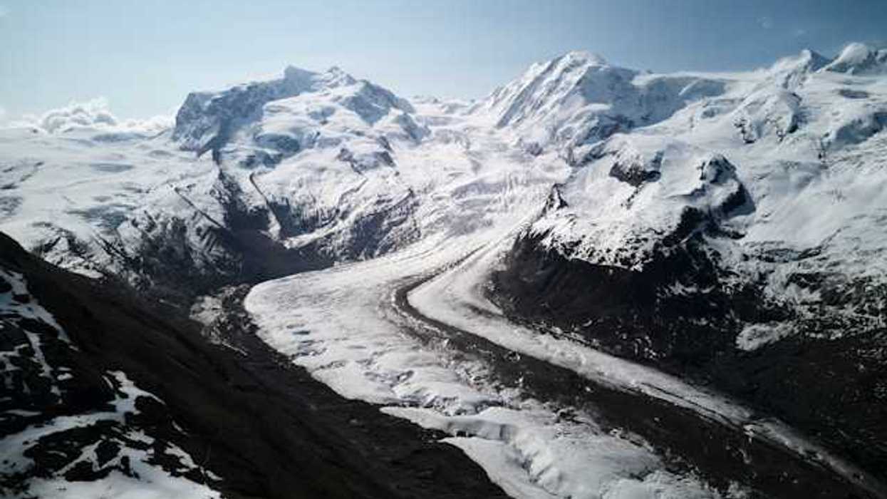 A glacier flowing down a valley under a snowy mountain range