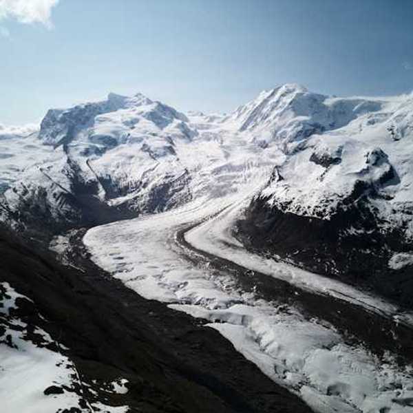 A glacier flowing down a valley under a snowy mountain range