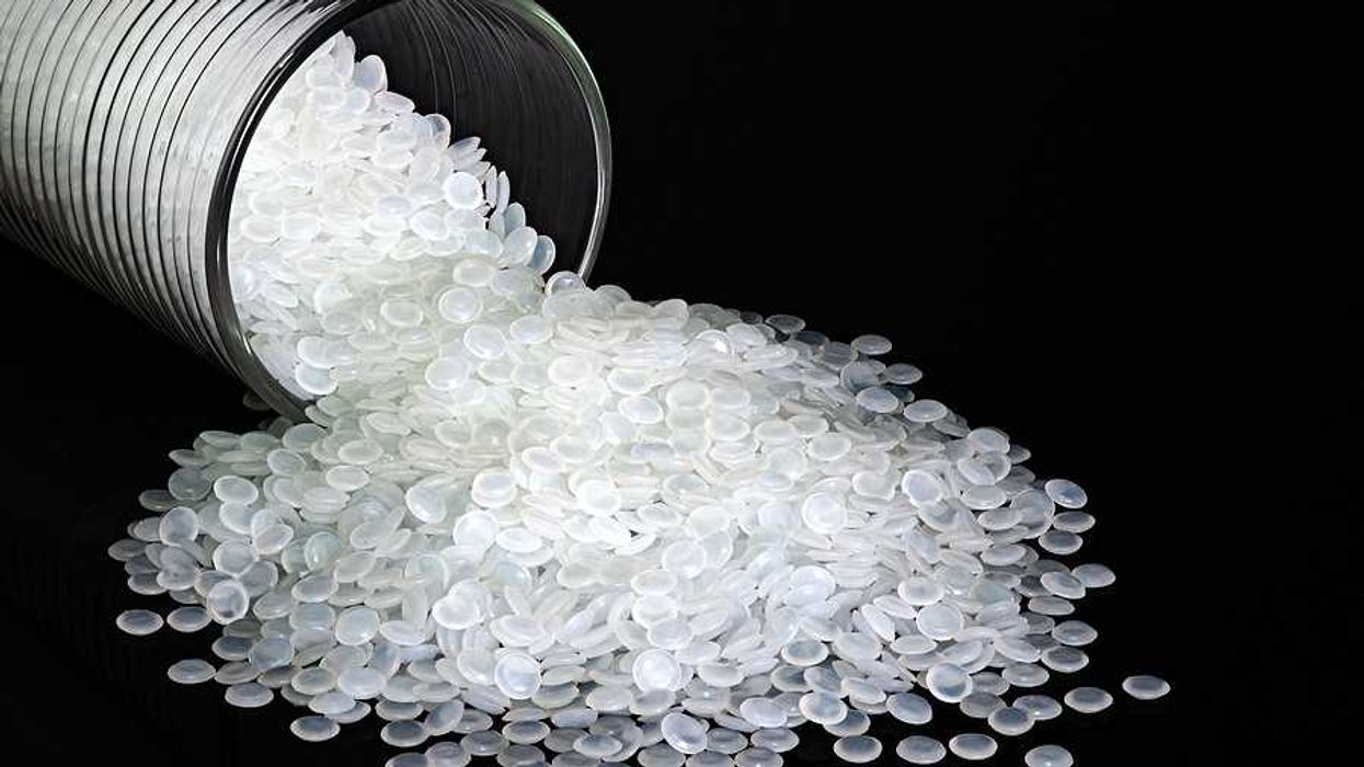 A glass container with round plastic pellets spilling from it against a black background