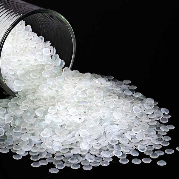 A glass container with round plastic pellets spilling from it against a black background