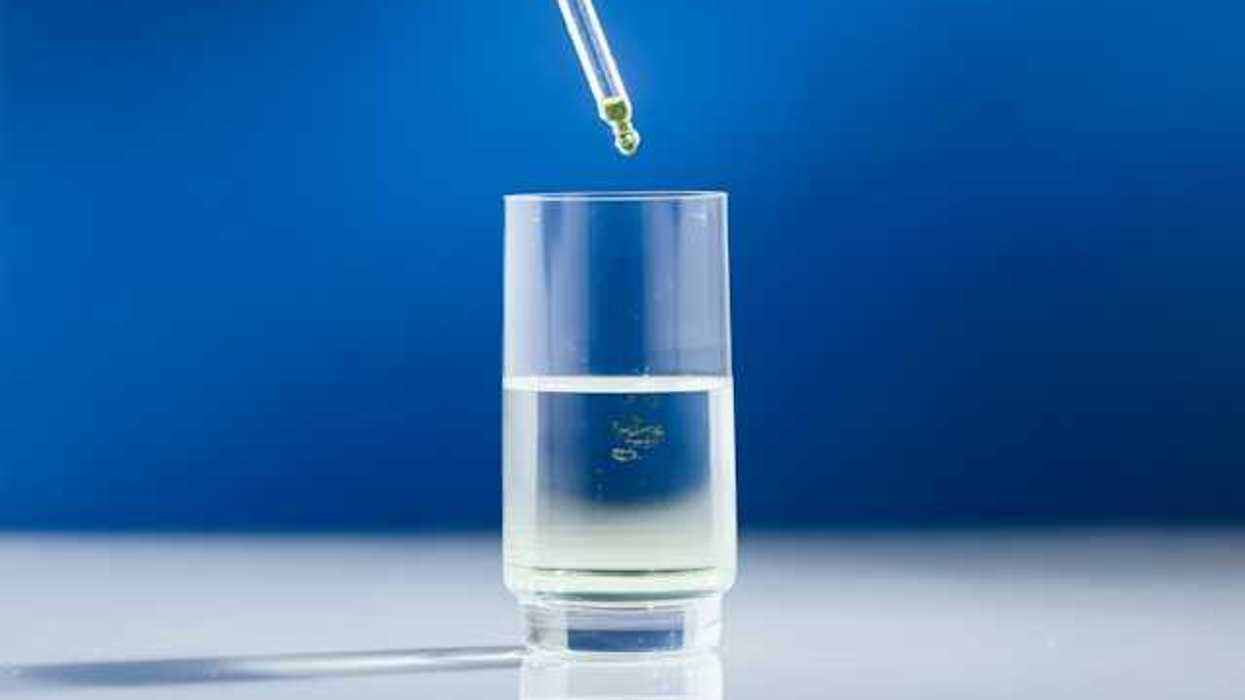 A glass of liquid with a pipette dropping yellow liquid into it
