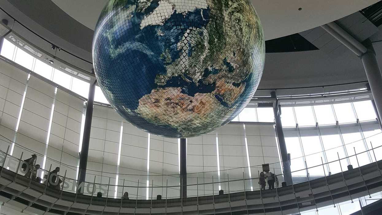 a globe suspended in an enormous room with people observing from a catwalk.