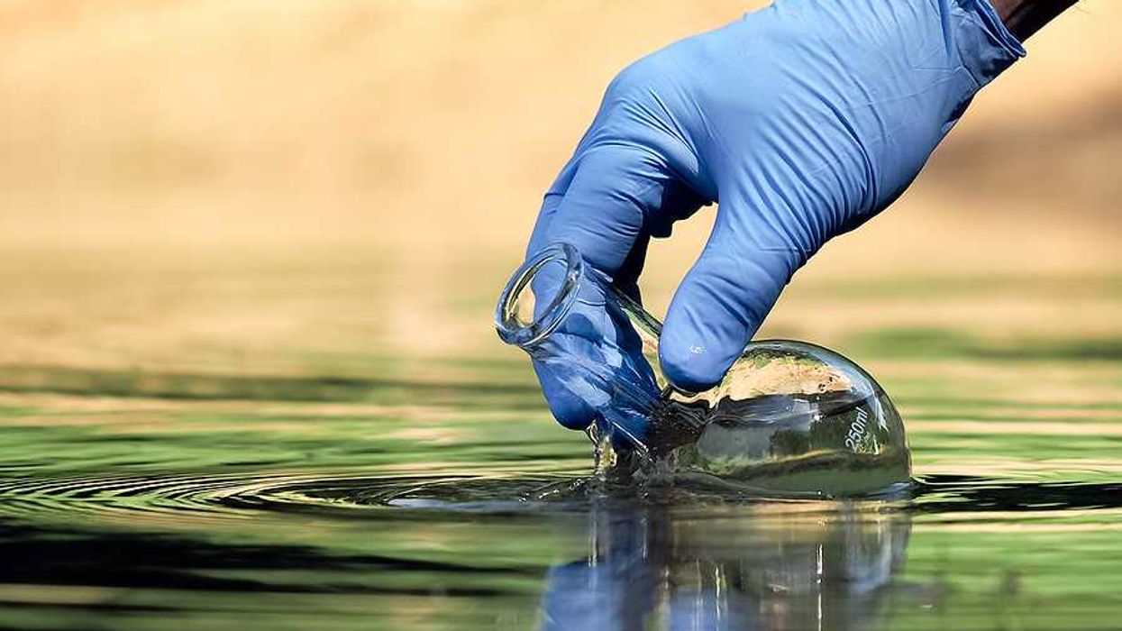 A gloved hand dipping a beaker into water in order to take a sample