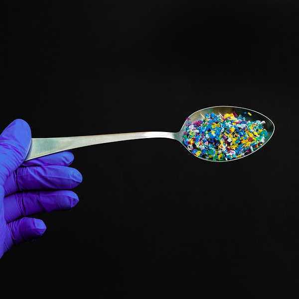 A gloved hand holding a spoon filled with tiny pieces of plastic