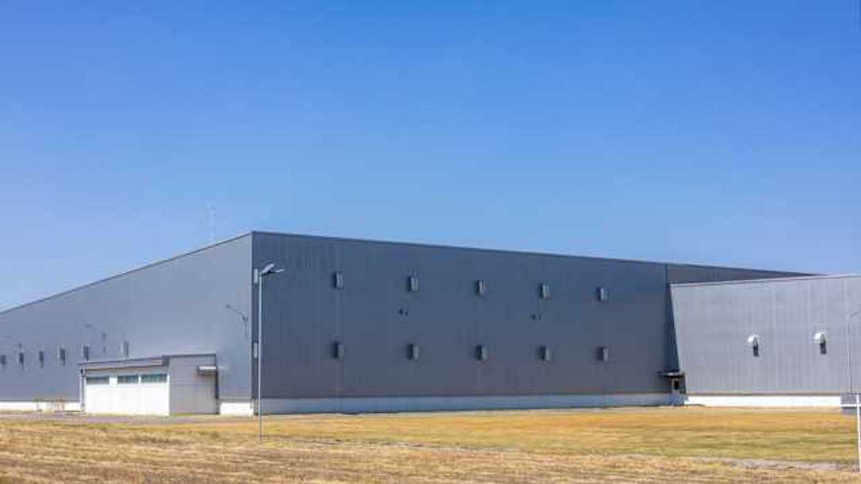 A gray warehouse type building on a brown field on a sunny day