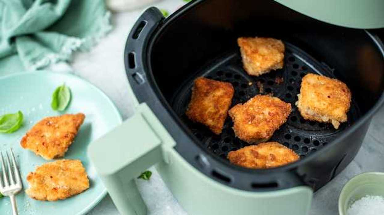 A green air fryer with some type of fried food in the basket