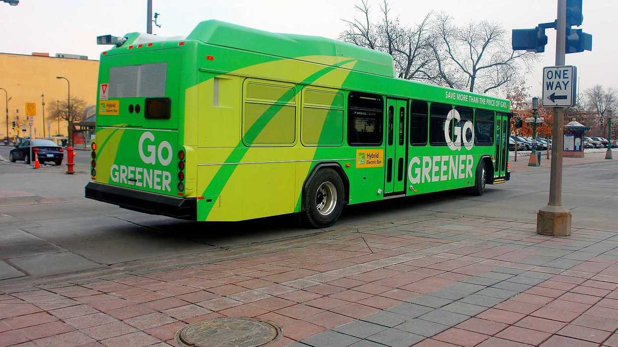 A green-colored electric bus in downtown Minneapolis advertising "Go GREENER"