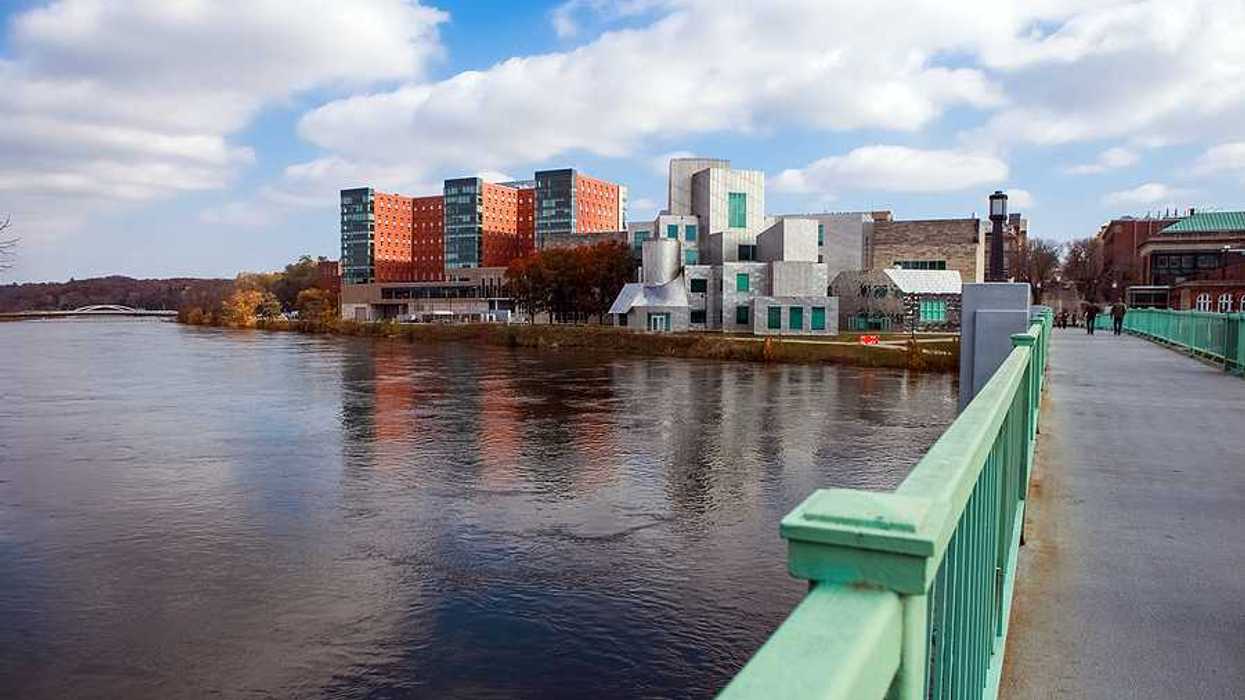 A green pedestrian bridge over a river with a small city skyline in the background