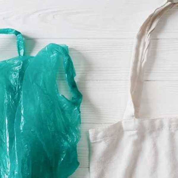 A green plastic bag next to a white tote against a wooden white background