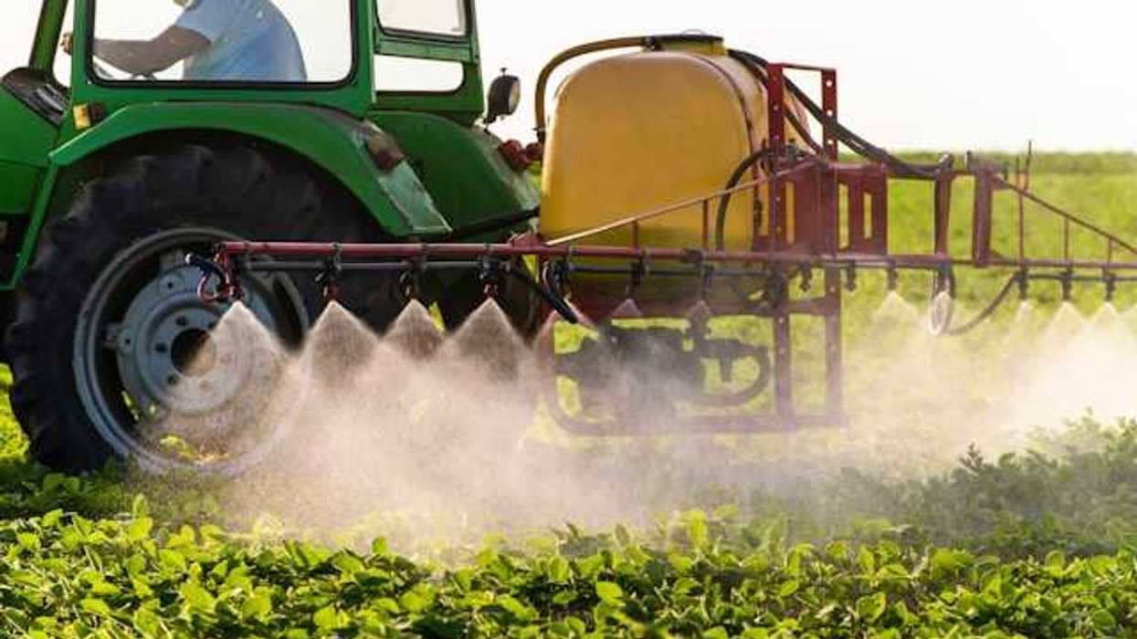 A green tractor applying pesticides to a farm field