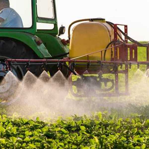 A green tractor applying pesticides to a farm field