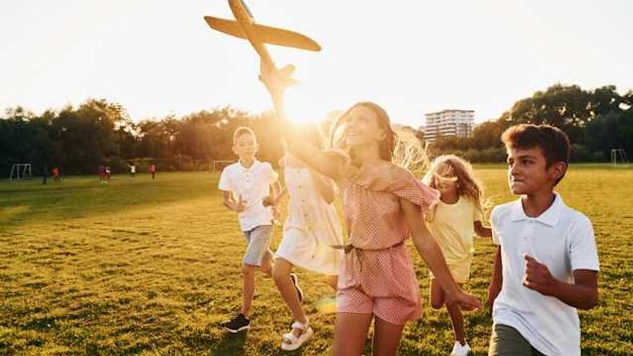 A group of children on a green lawn running with a toy airplane