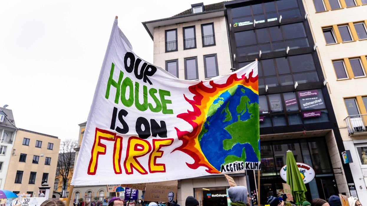 A group of climate protesters holding a sign that says our house is on fire.