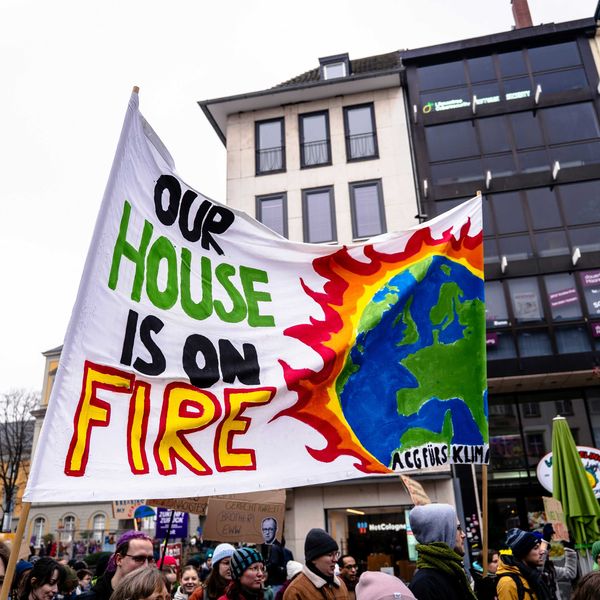 A group of climate protesters holding a sign that says our house is on fire.
