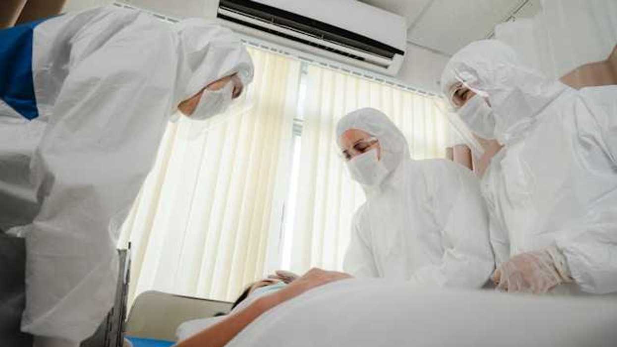 A group of masked health professionals standing over a patient's bed