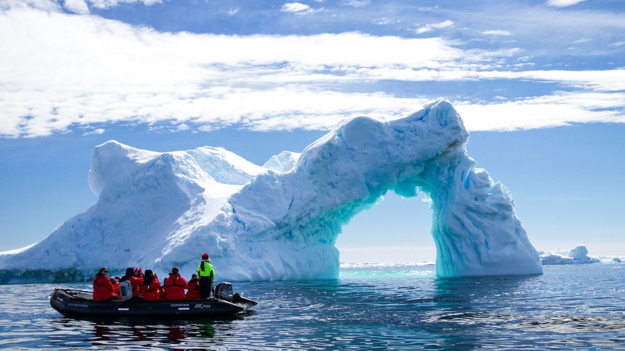 a group of people in a small boat in front of an iceberg.