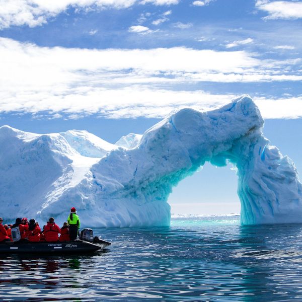 a group of people in a small boat in front of an iceberg.