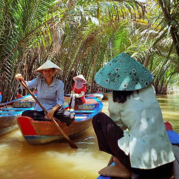 A group of people in hats riding on top of small rowboats on a river.