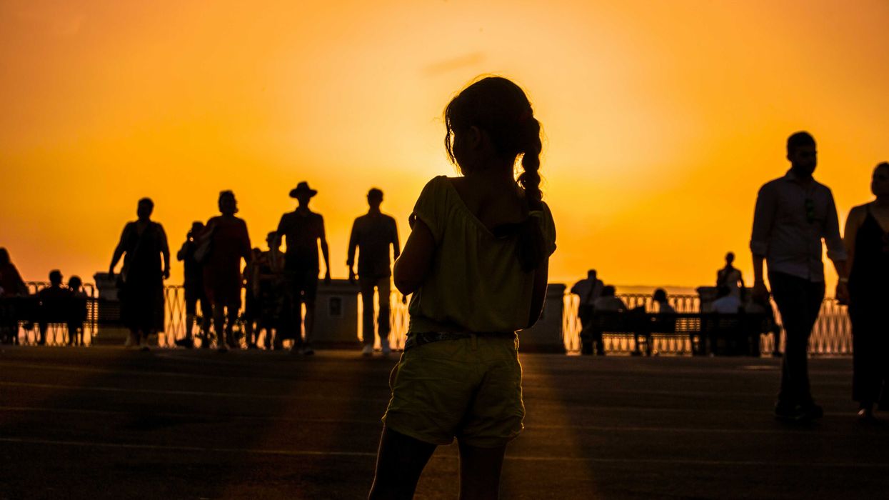 A group of people silhouetted against an orange sun-tinged sky